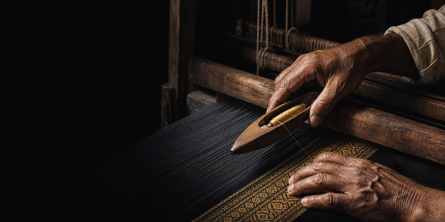 A master weaver guiding black silk through a traditional handloom